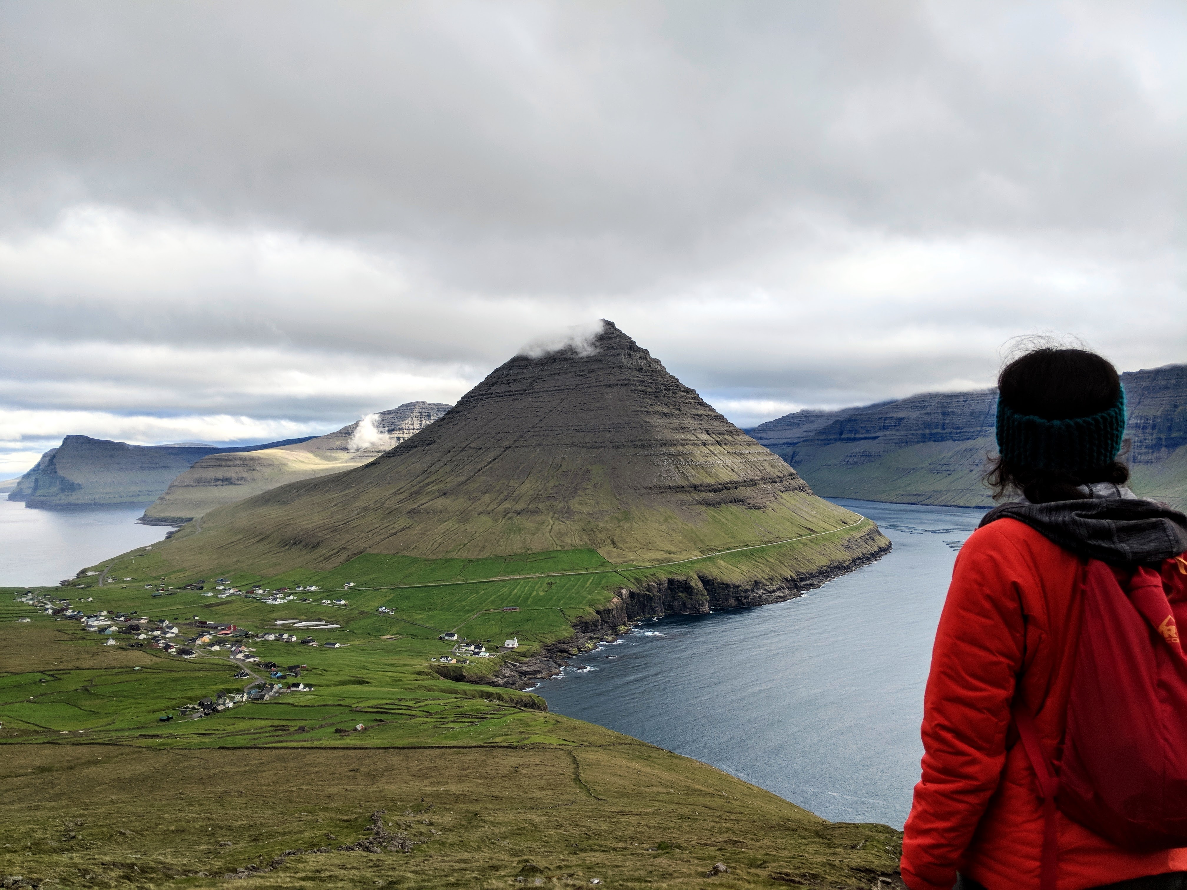 Julie overlooking a fjord and village in the Faroe Islands, wearing a red jacket